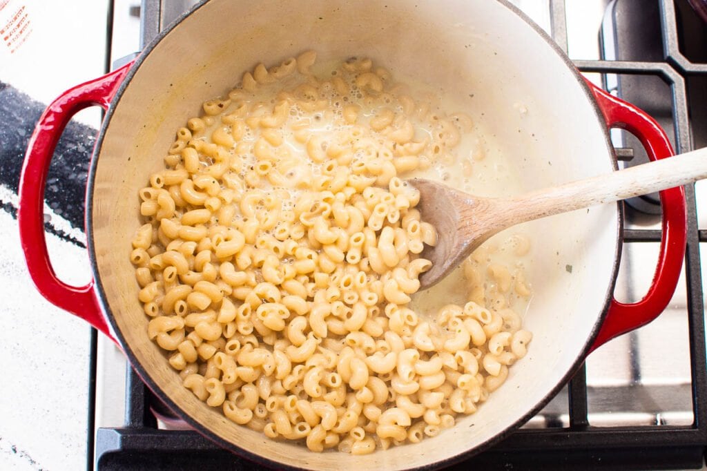 Elbow macaroni cooking in broth and milk in a pot with wooden spoon.