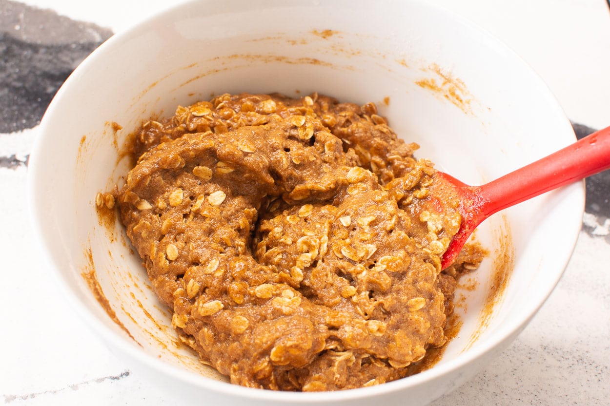 Pumpkin cookies dough in a white bowl with red spoon.