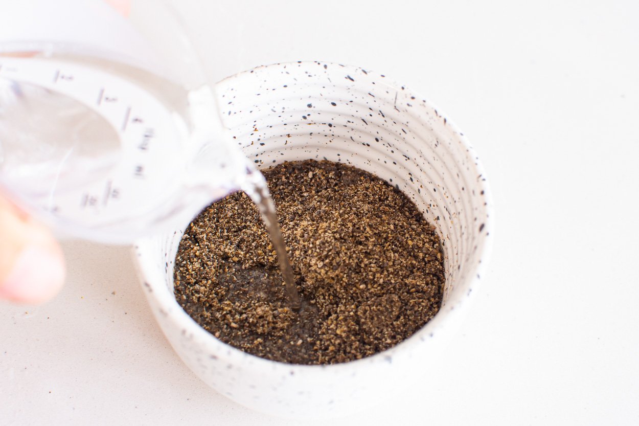 Pouring water over ground chia in white bowl.