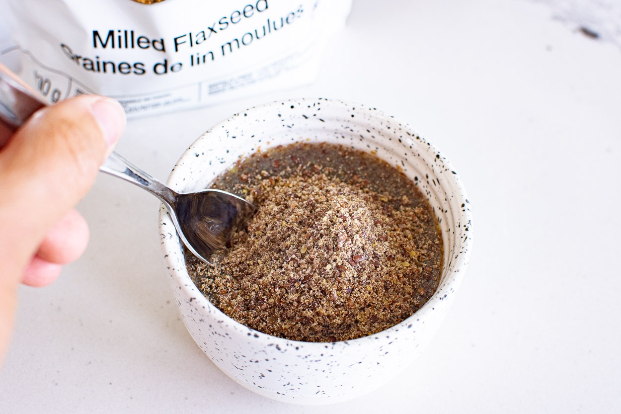 Ground flaxseed and water in a bowl being stirred with a spoon.