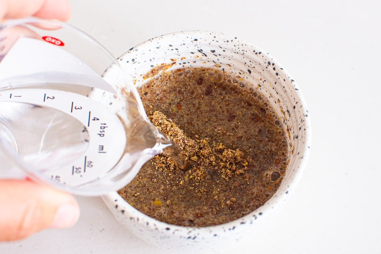 Water poured from measuring cup into bowl of ground flaxseeds.