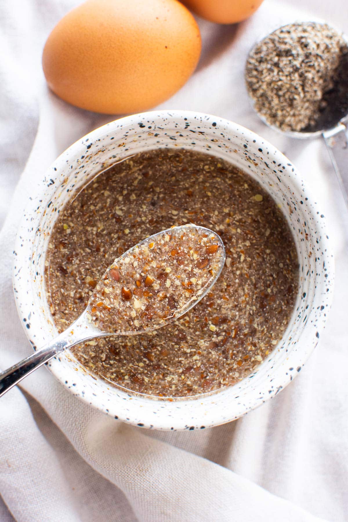 Flaxseed egg in a bowl and on a spoon. Brown eggs in background.