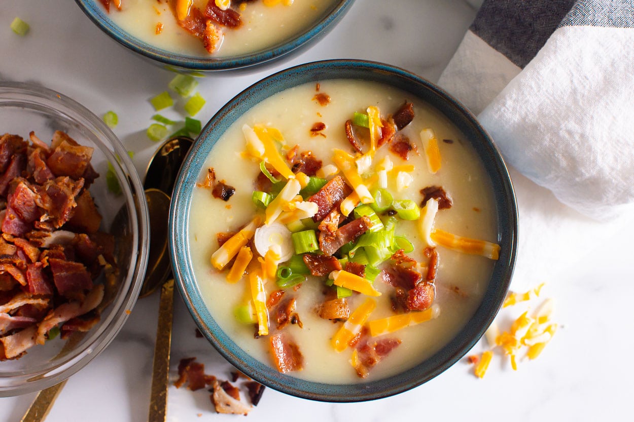 Potato soup in a bowl with bacon beside it for garnish.