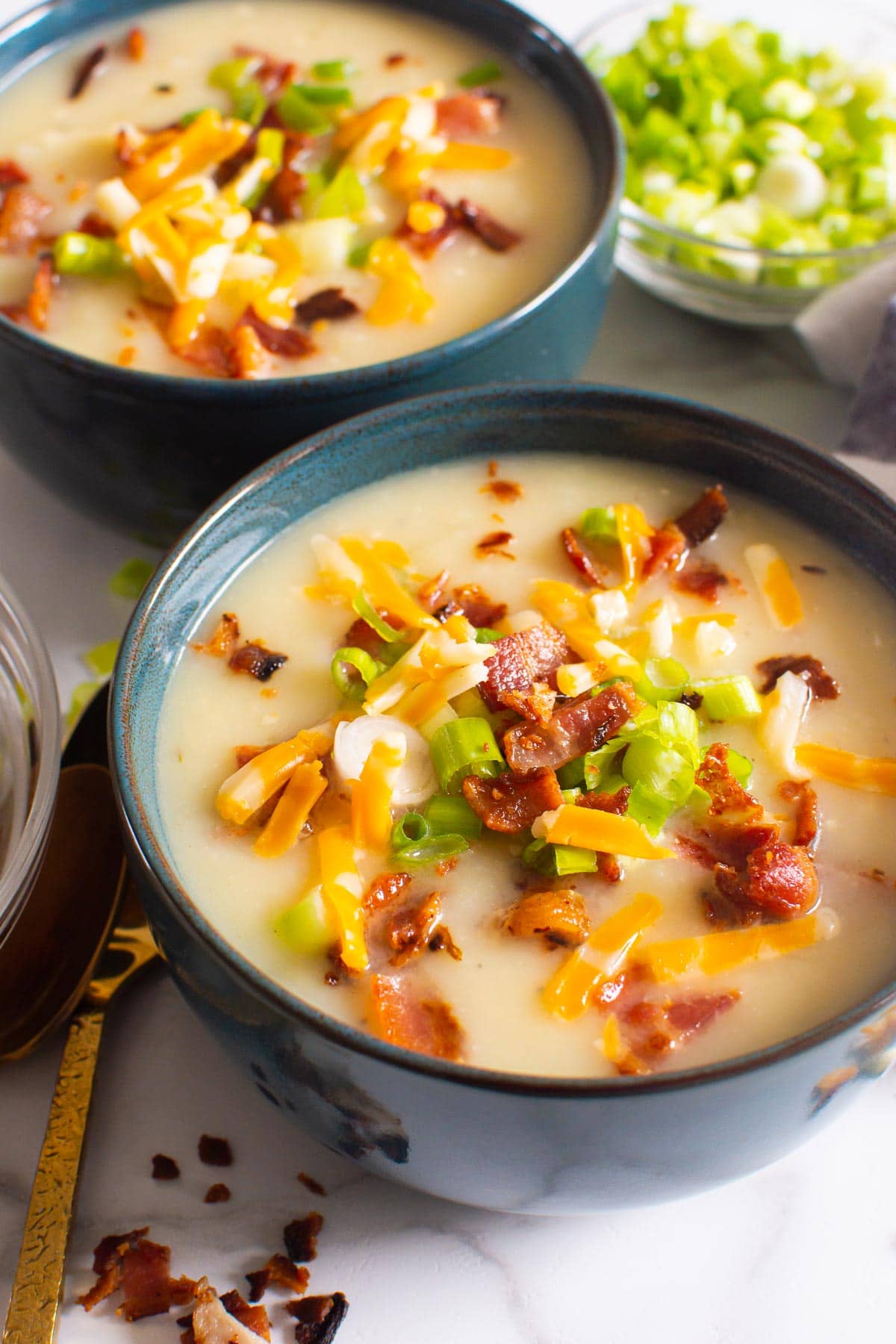 Instant Pot potato soup garnished with green onion, cheese, and bacon in bowls.