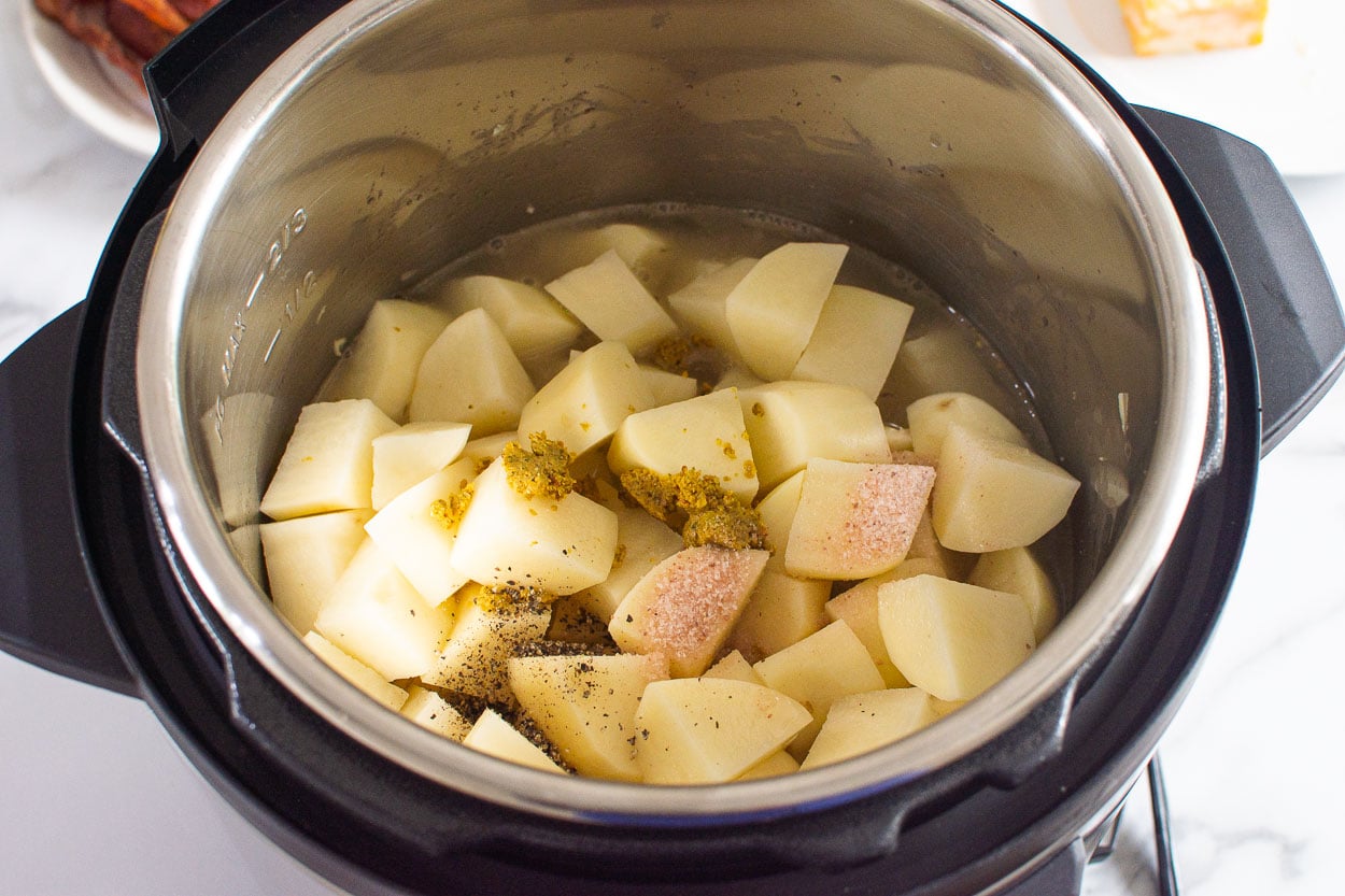 Cubed potatoes with seasonings and broth in pressure cooker pot.