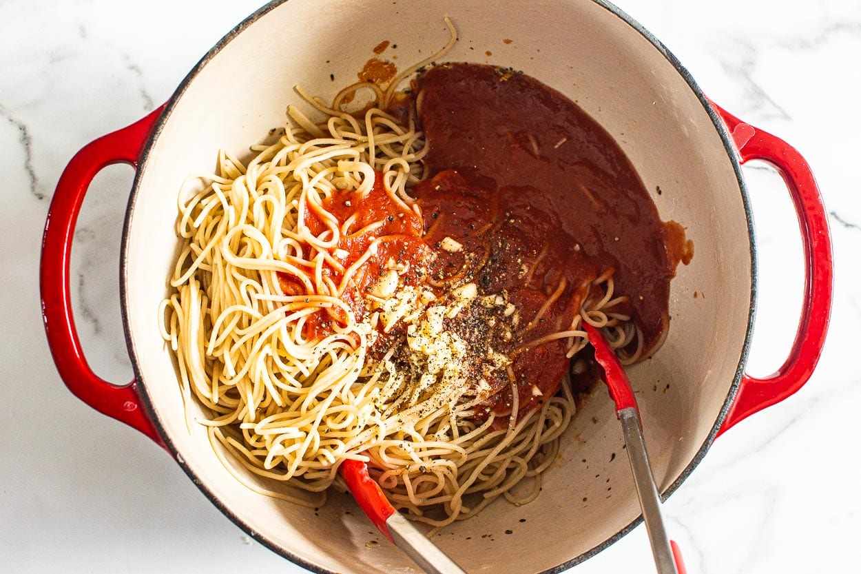 Garlic, pepper, and tomato sauce with spaghetti noodles in a pot.
