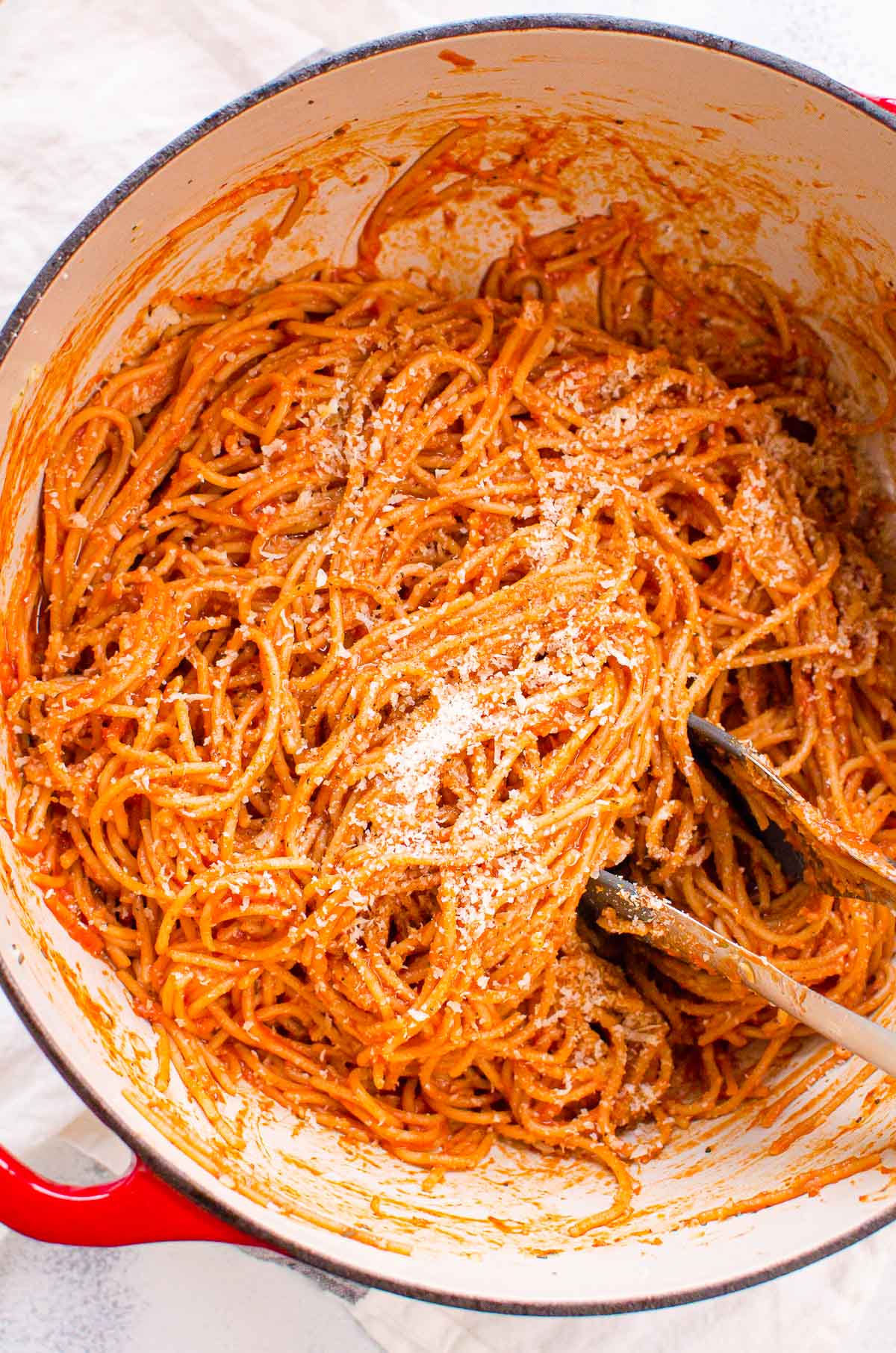 Simple spaghetti recipe garnished with parmesan cheese in a pot with tongs.