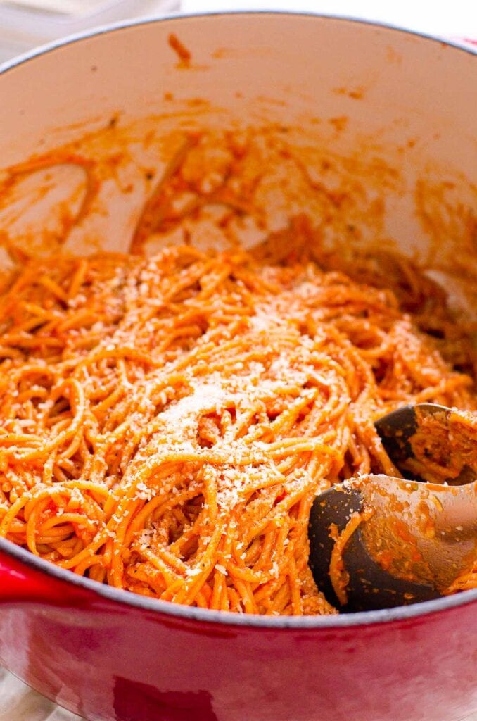 Spaghetti in a pot with cheese and tongs.