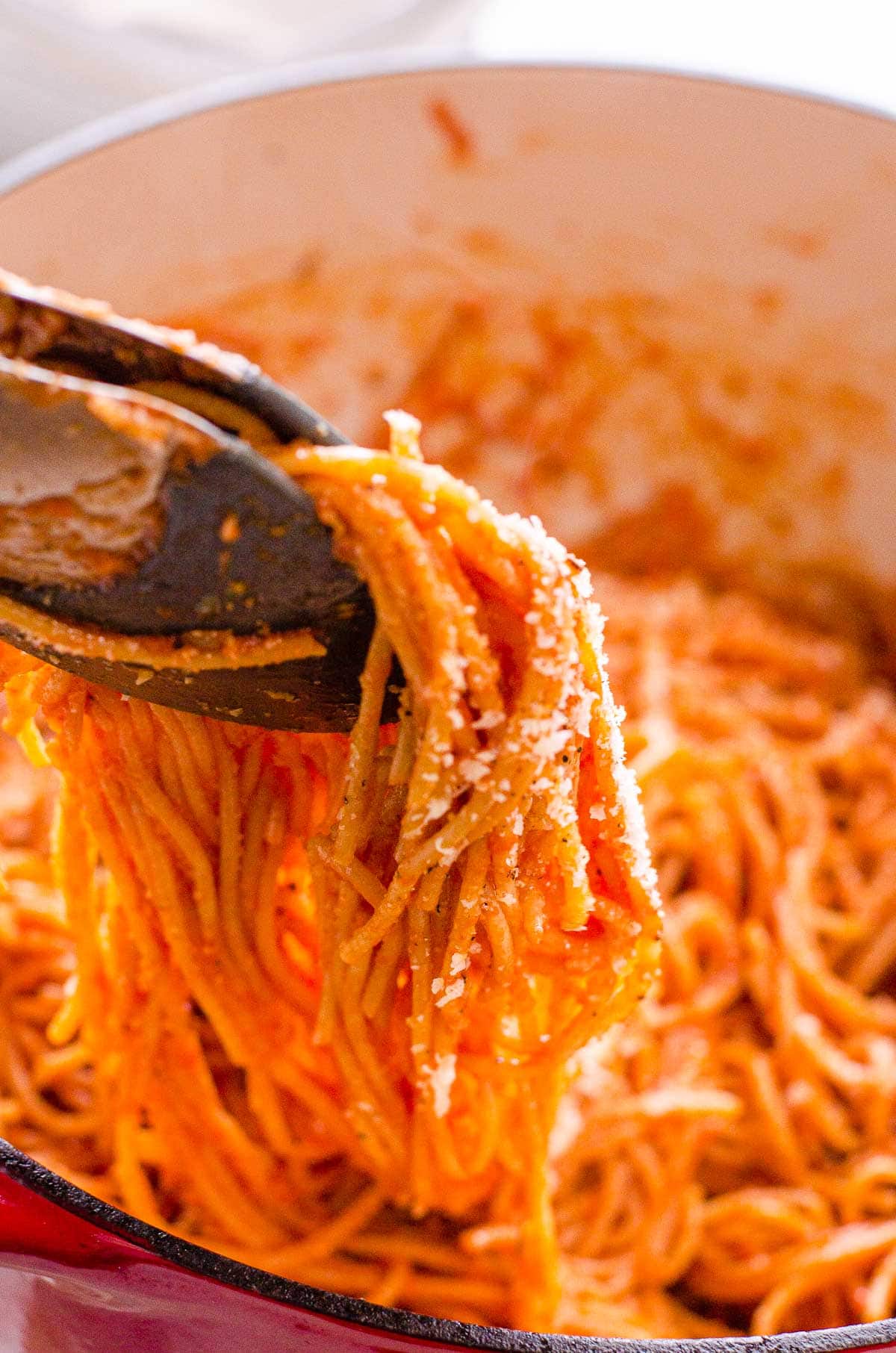 Easy spaghetti recipe garnished with parmesan cheese held over the pot with tongs.