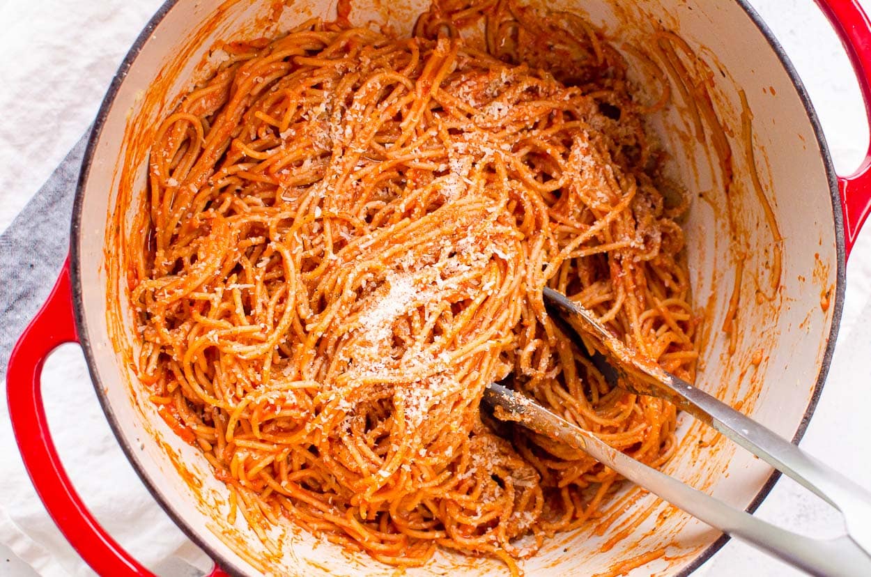 Easy spaghetti recipe in red pot with Parmesan and serving tongs.