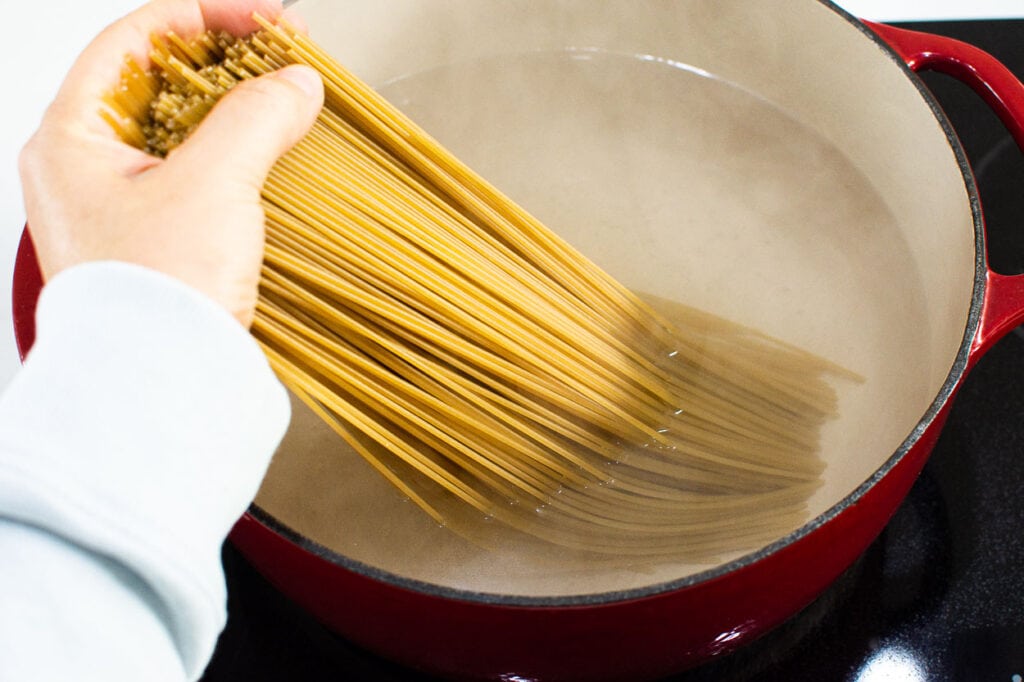 adding spaghetti to a pot of water