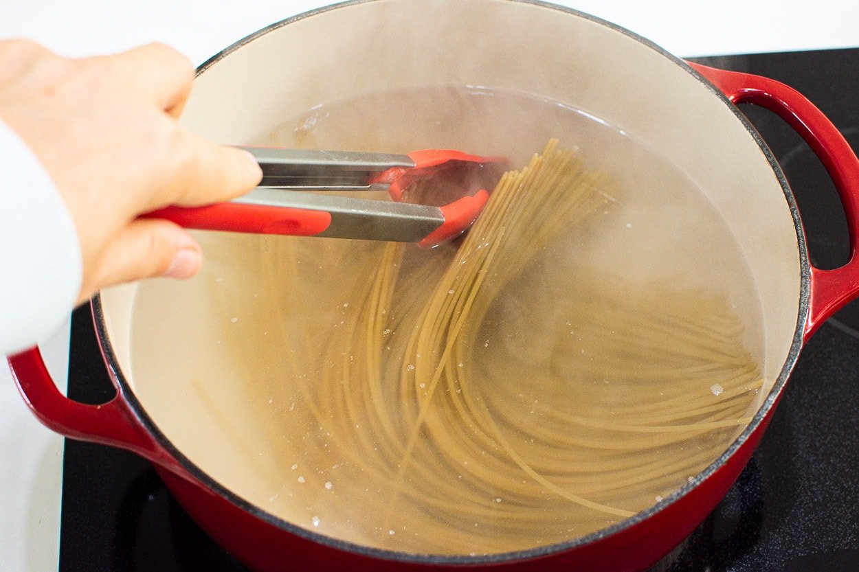 Separating spaghetti strands with tongs.