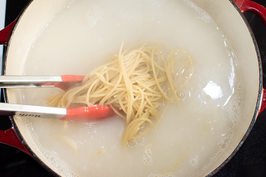 Tongs being used to get cooked spaghetti out of pot with water.