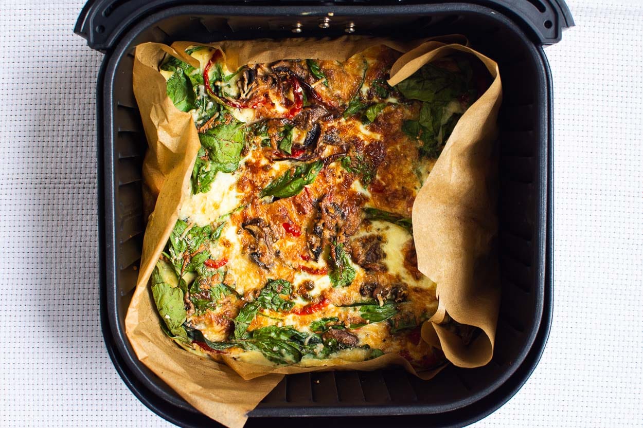 Cooked breakfast casserole in air fryer basket lined with parchment.