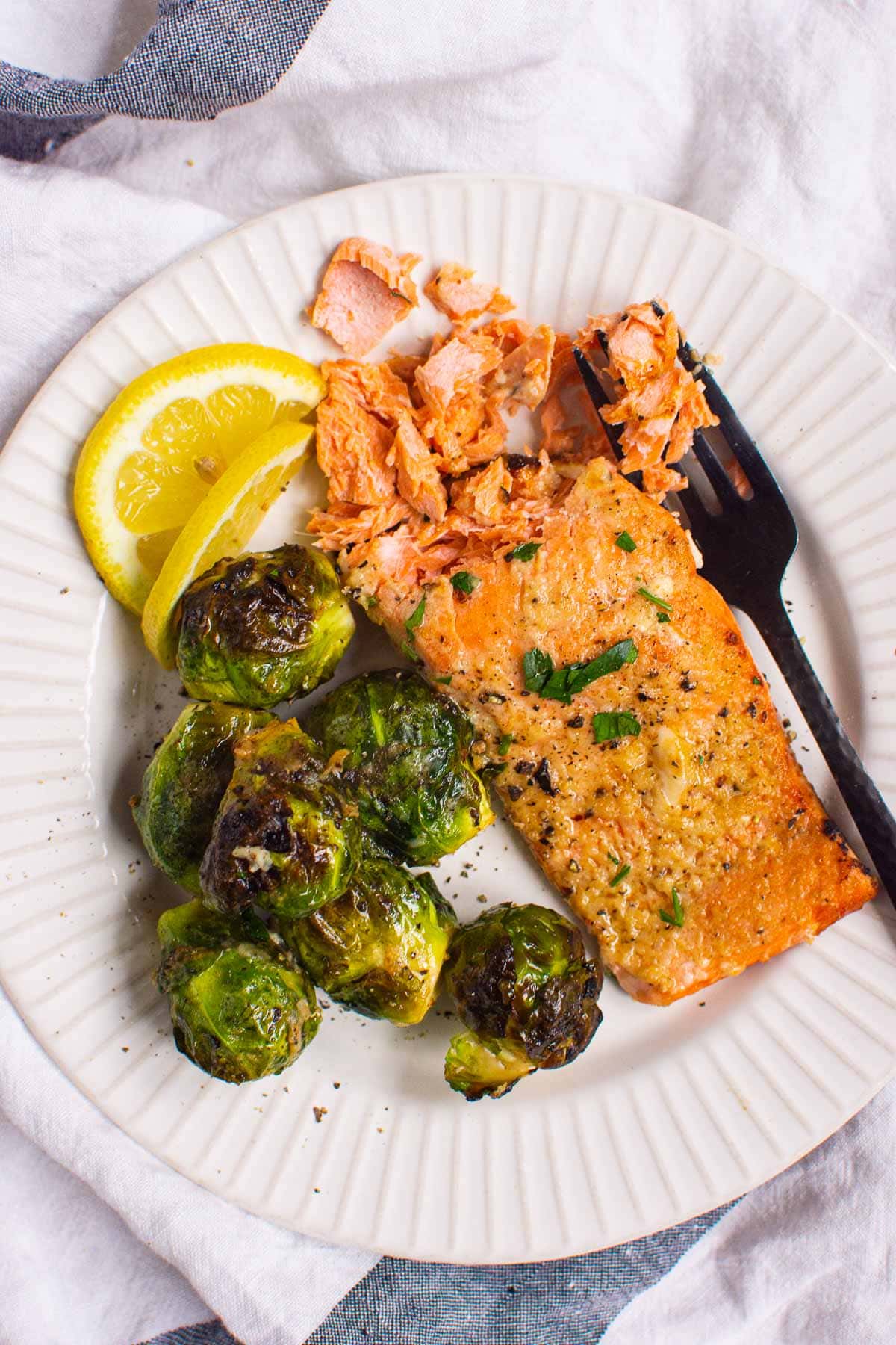 Air fryer salmon with brussels sprouts on a plate with a lemon wedge.
