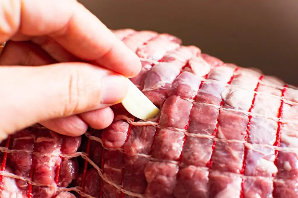 inserting garlic into a lamb roast