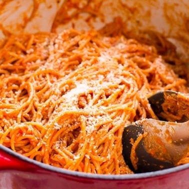 Easy spaghetti recipe in red pot with tongs and Parmesan cheese.