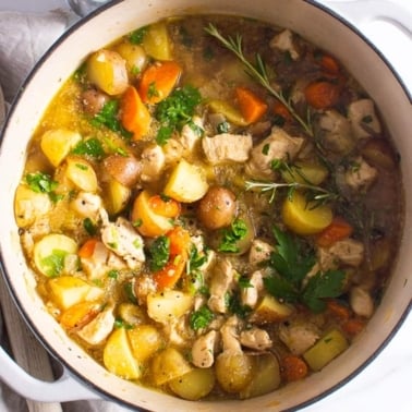 chicken stew with potatoes in large pot with rosemary sprig