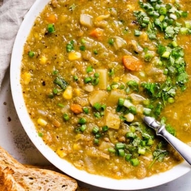 Slow cooker lentil soup with herbs in a bowl with a spoon and bread.