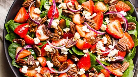 Strawberry spinach salad with feta cheese in a bowl with utensils.