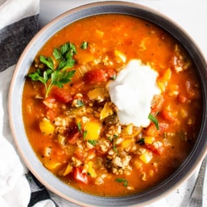 Stuffed bell pepper soup served in a bowl with dollop of sour cream and garnished with parsley.