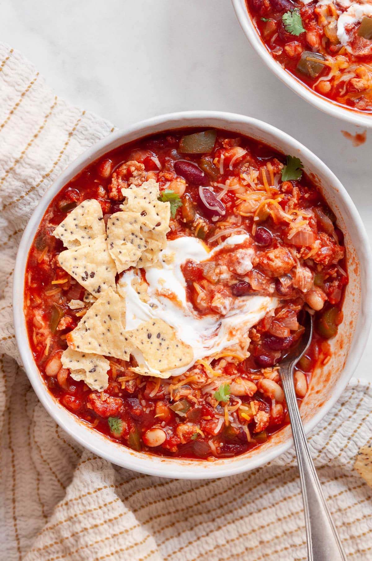 View from above of turkey chili with crushed chips and sour cream mixed with a spoon in a bowl.