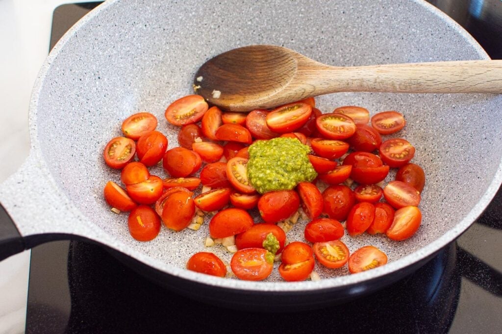 Halved tomatoes and pesto in skillet.