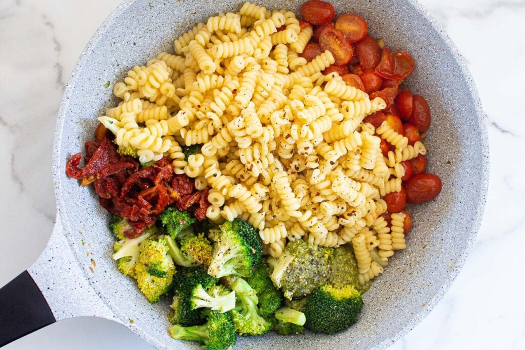 Pasta, broccoli, tomatoes and sun dried tomatoes in skillet.