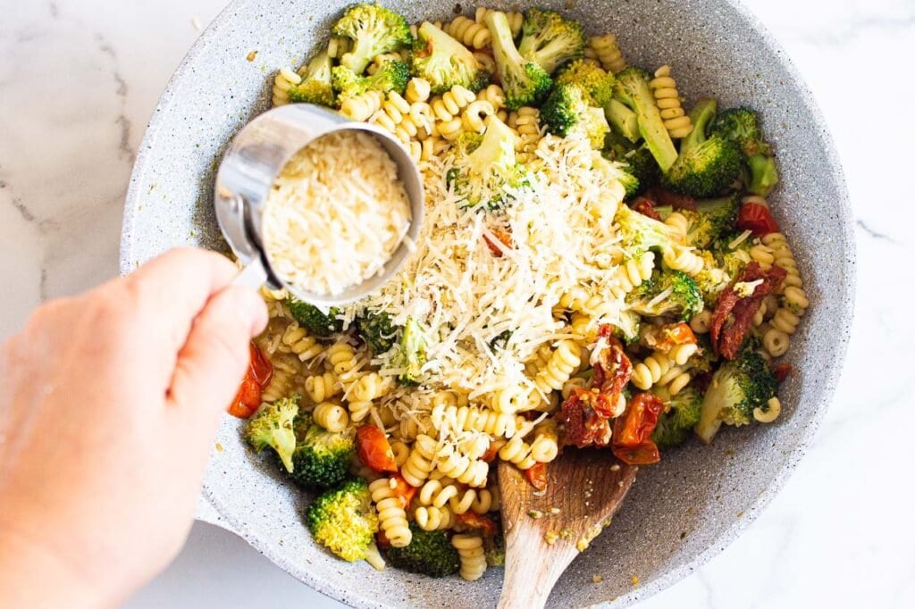Adding parmesan cheese into pasta and veggies in skillet.