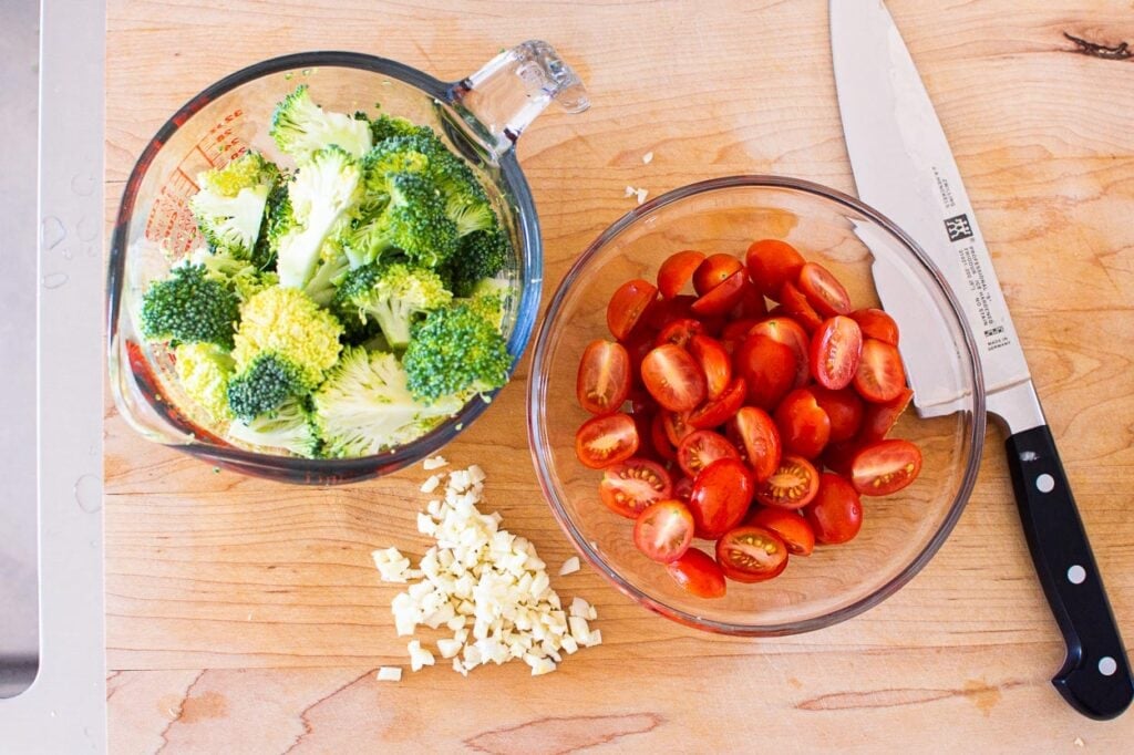 Broccoli and tomatoes on cutting board with garlic.