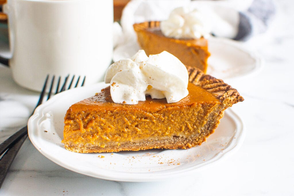homemade pumpkin pie sliced onto a plate with whipped cream