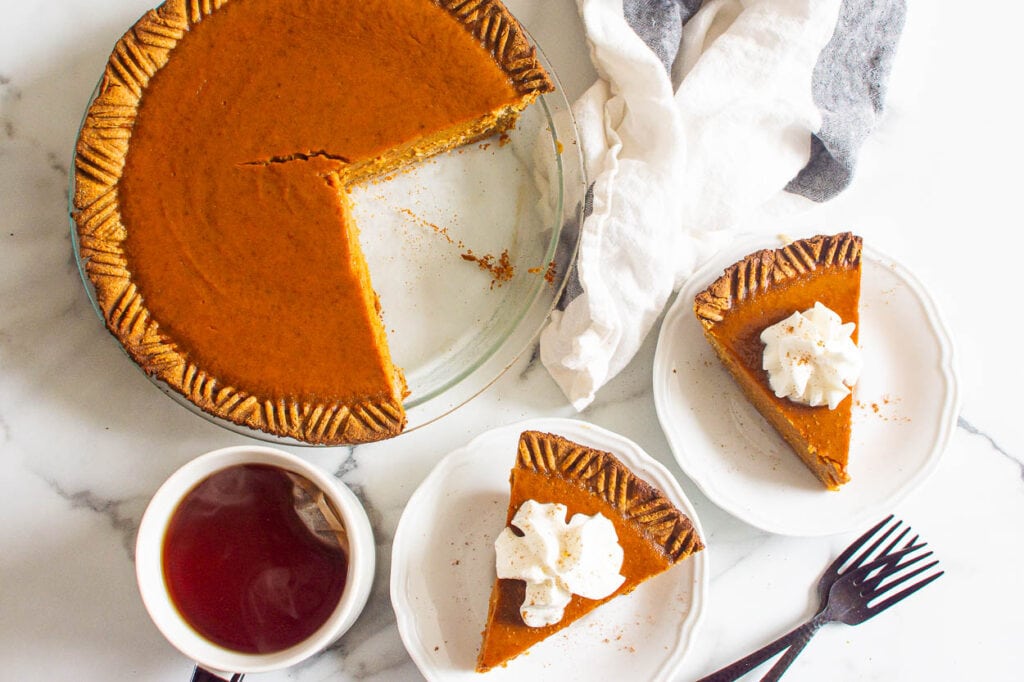 low sugar pumpkin pie with two slices cut on plate with forks and a cup of tea