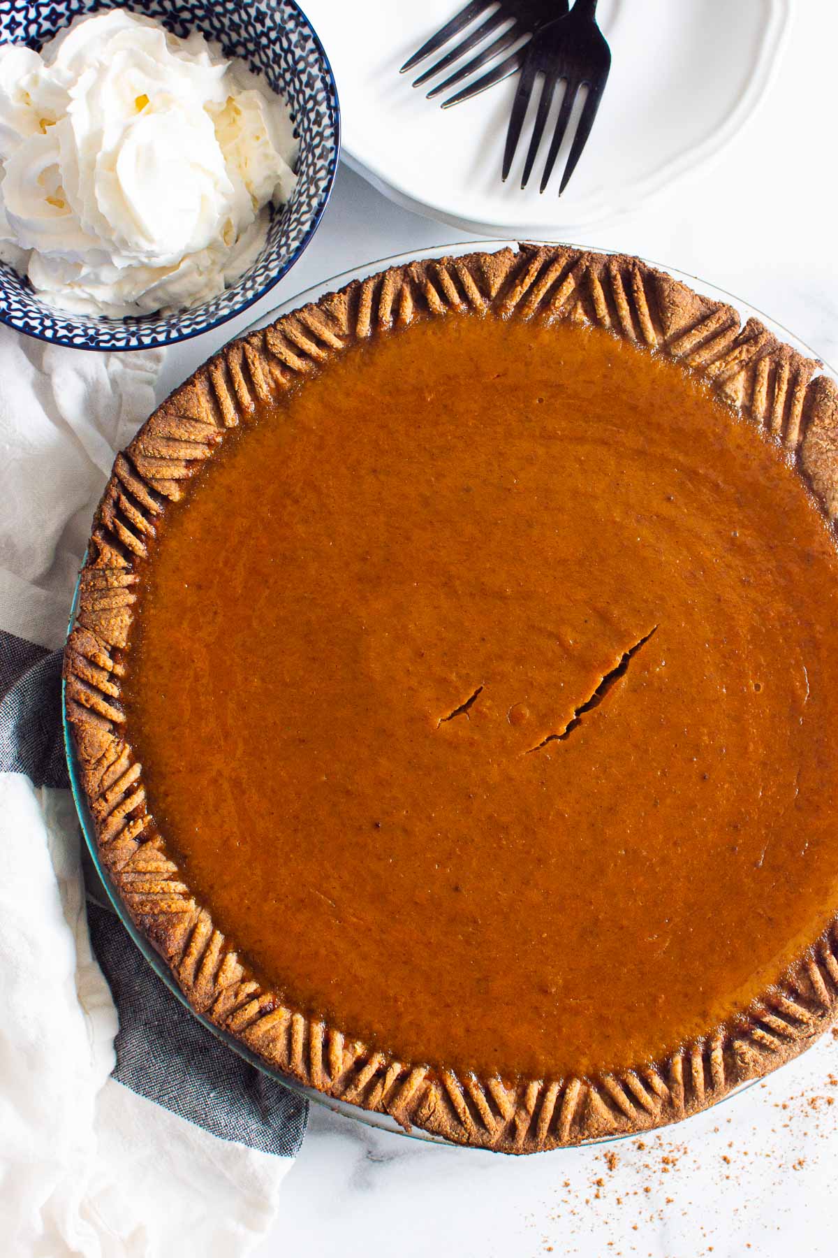 homemade pumpkin pie with a bowl of whipped cream and forks