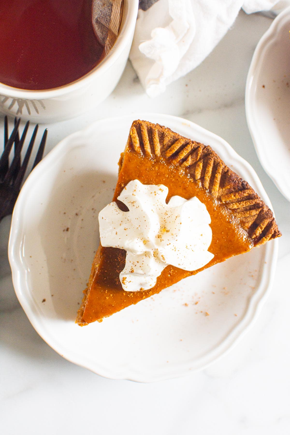 A slice of healthy pumpkin pie on a plate topped with whipped cream and served with tea. 