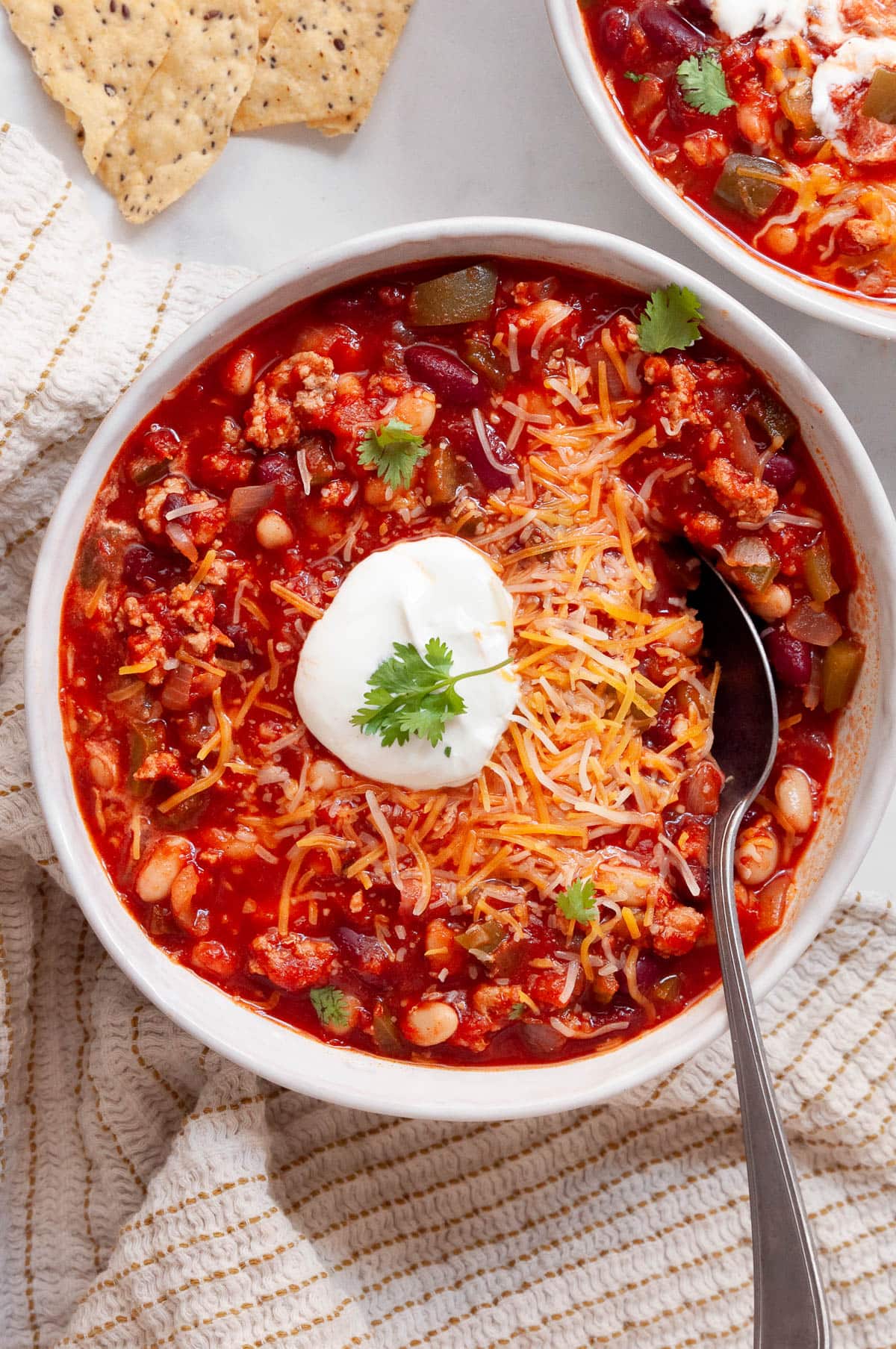 Healthy turkey chili with sour cream, cheese and cilantro in a bowl with spoon.