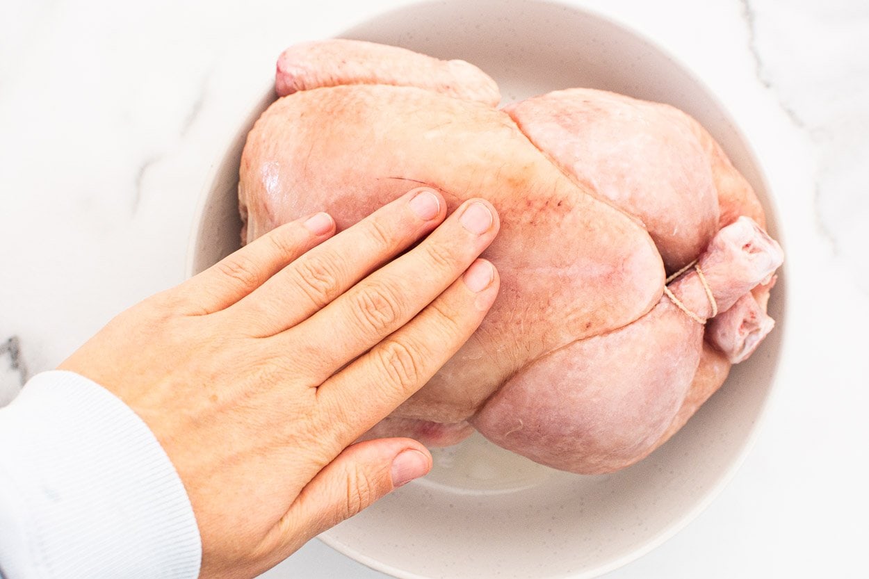 A hand rubbing chicken on a plate.