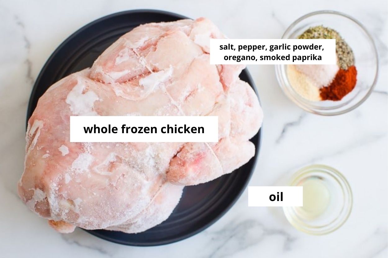 Whole frozen chicken on a plate, spices and oil in bowl.