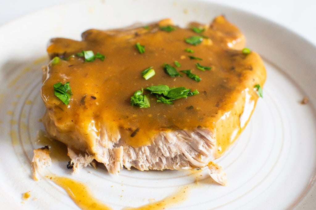 instant pot pork chop cut into to show tenderness and on a plate with garnish
