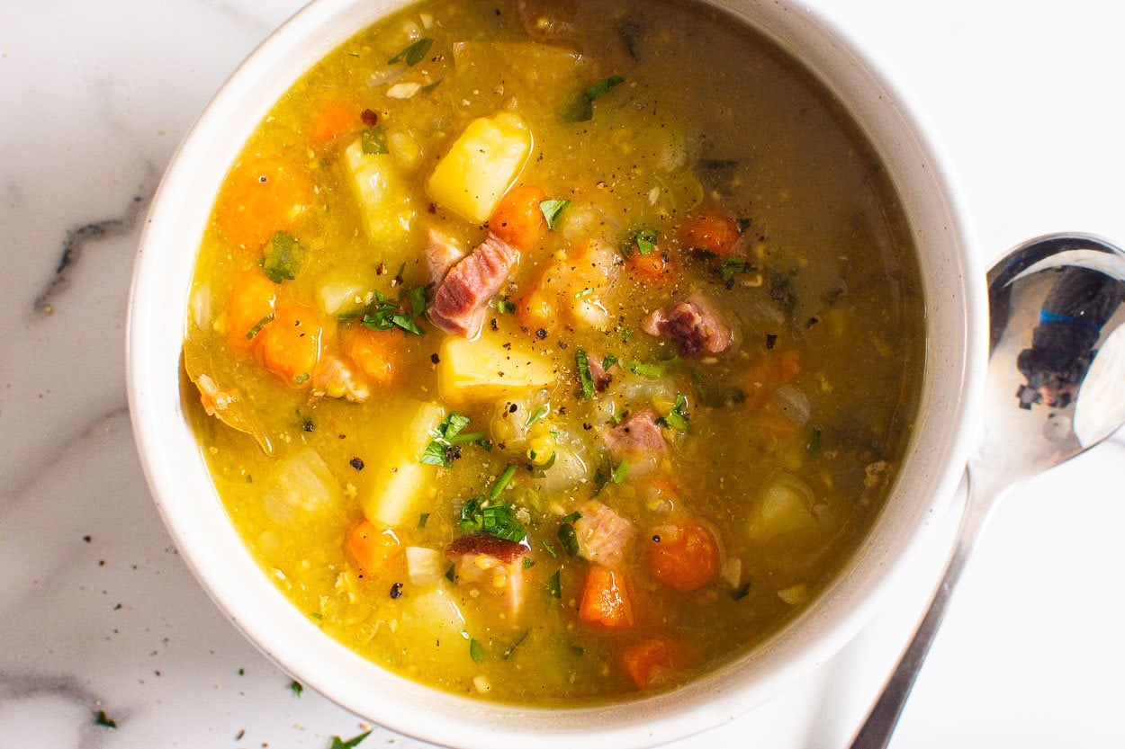 Instant pot split pea soup with ham, potatoes, carrots, and parsley served in white bowl with a spoon.