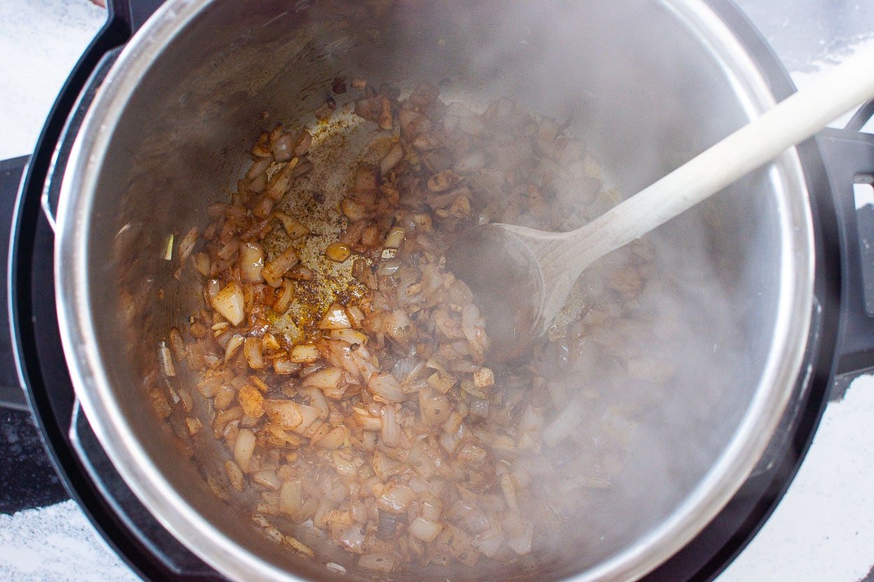 Stirring sauteed onion, garlic and spices in Instant Pot with wooden spoon.