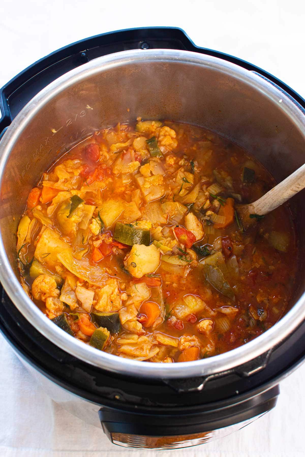 Instant Pot vegetable soup in the pressure cooker with a wooden spoon.