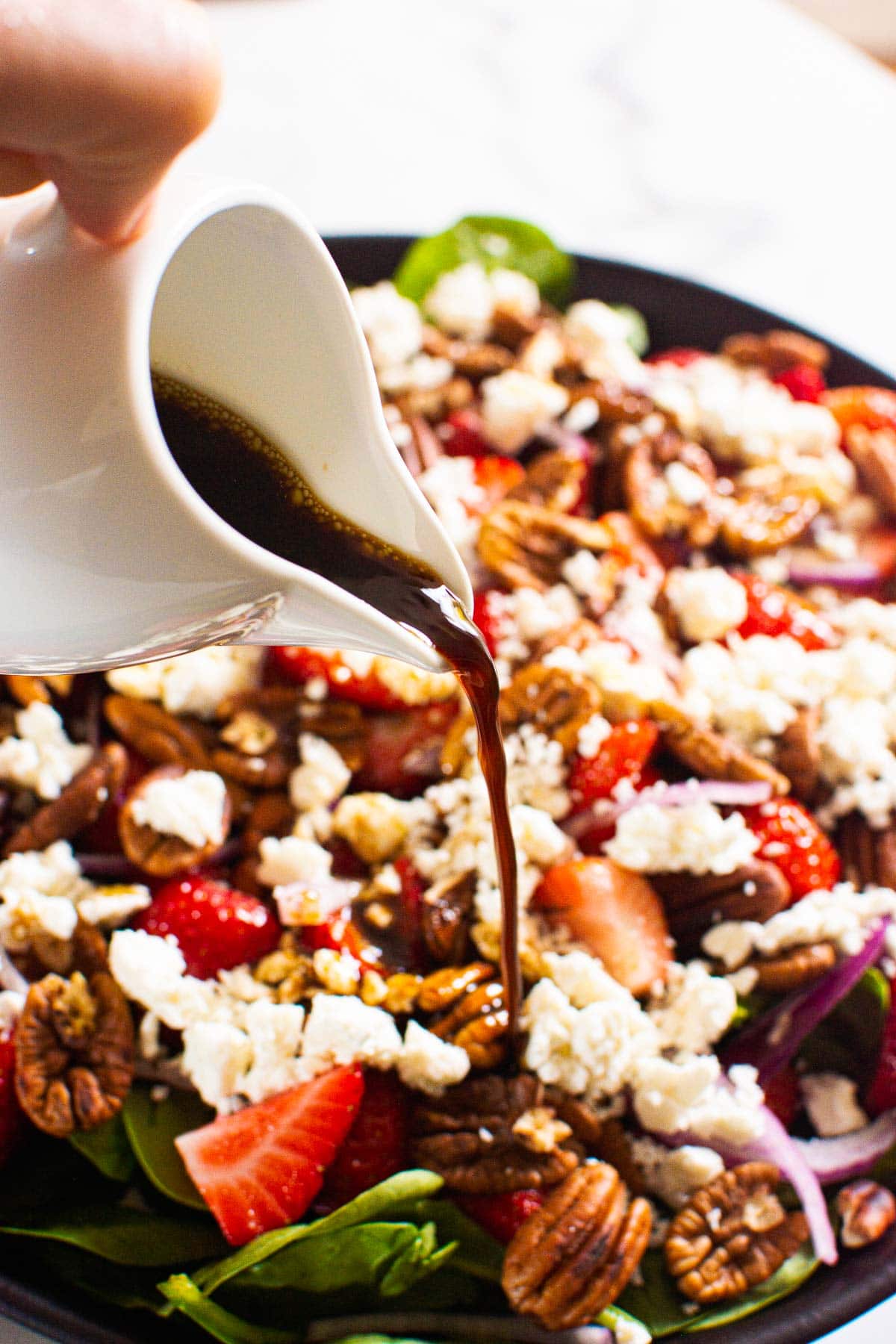 Strawberry spinach salad with balsamic dressing being poured on salad.