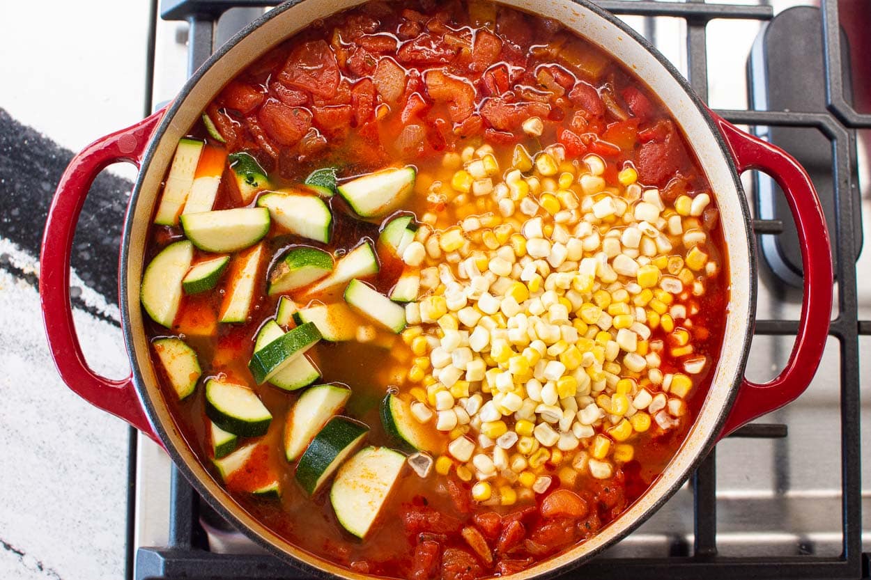 Zucchini and corn added to a pot of soup on the stove. 