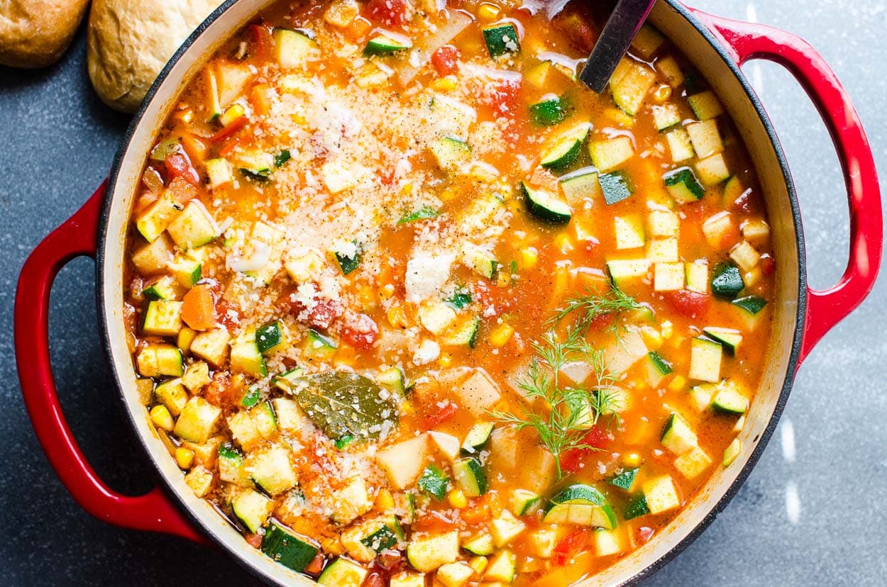 Veggie soup in red Dutch oven and bread rolls nearby.