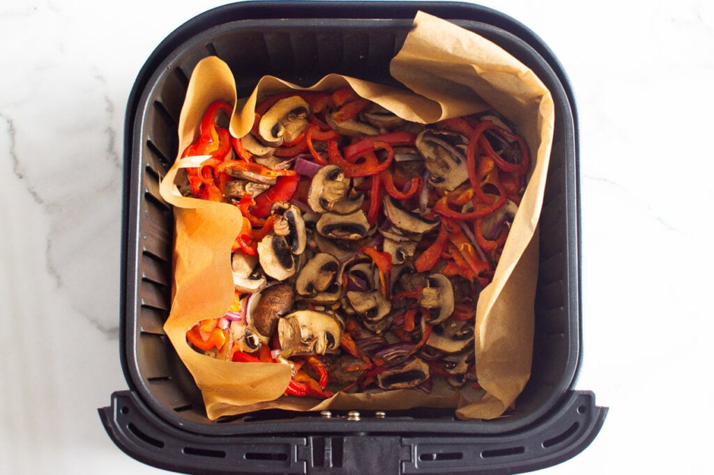 Cooked mushrooms, bell pepper and red onion in air fryer basket.