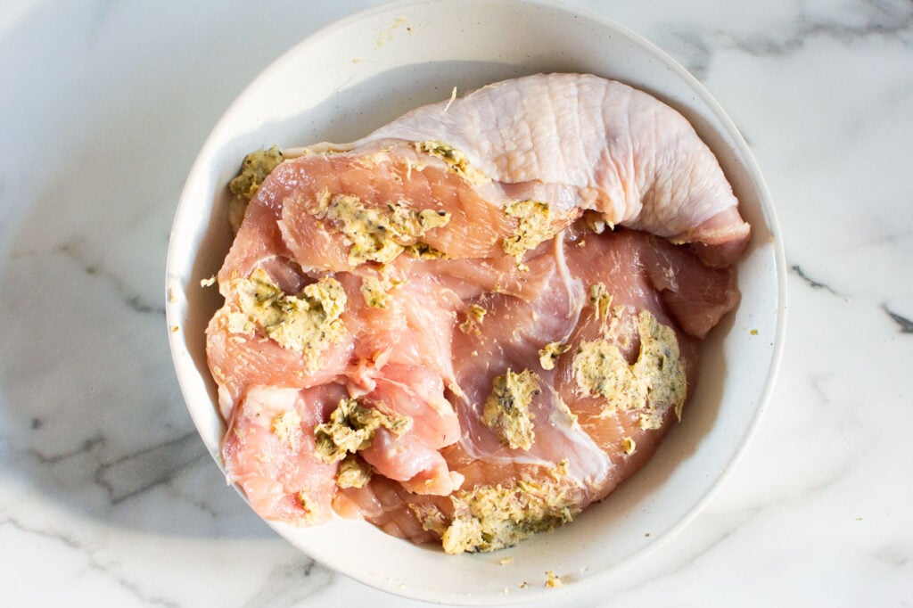 Turkey breast being patted by butter herb mixture.