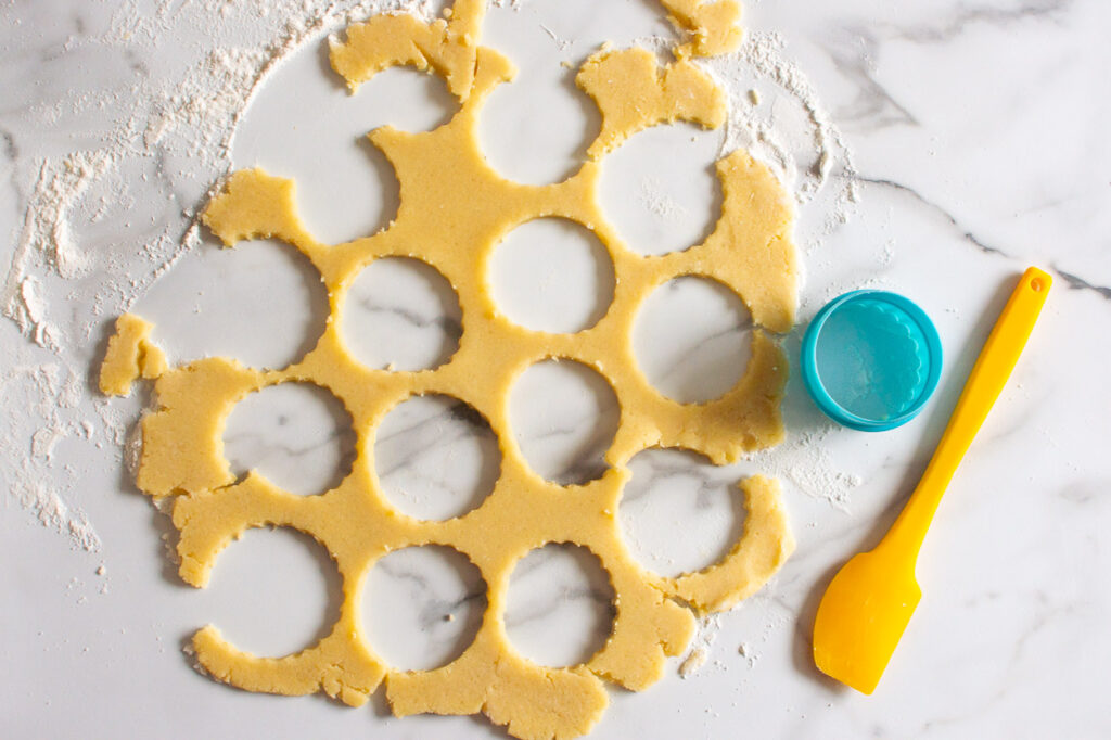 Cookie dough with round cut outs, a blue cookie cutter and yellow spatula.
