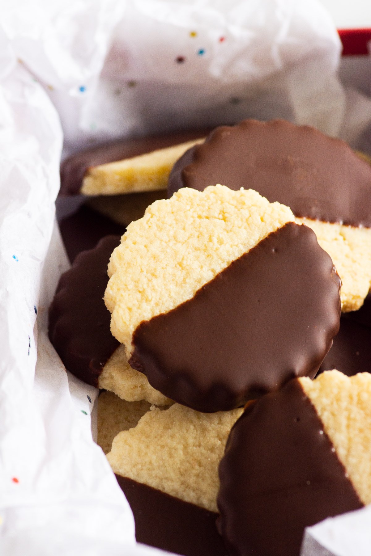 Chocolate dipped shortbread cookies laying on white tissue paper in a box.