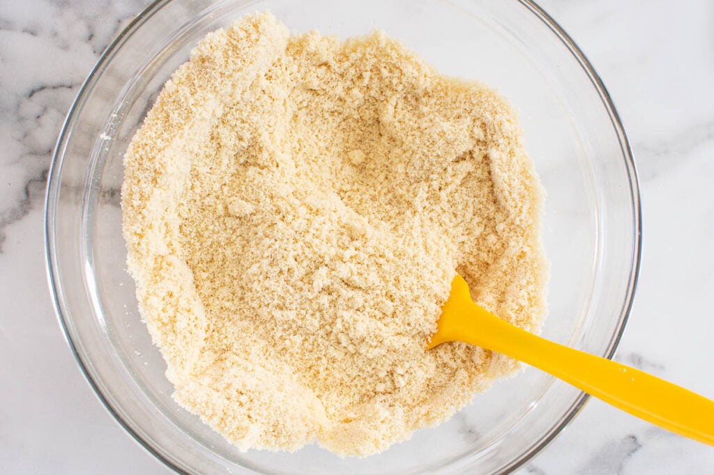 Mixing flour and baking soda in glass bowl with yellow spatula.