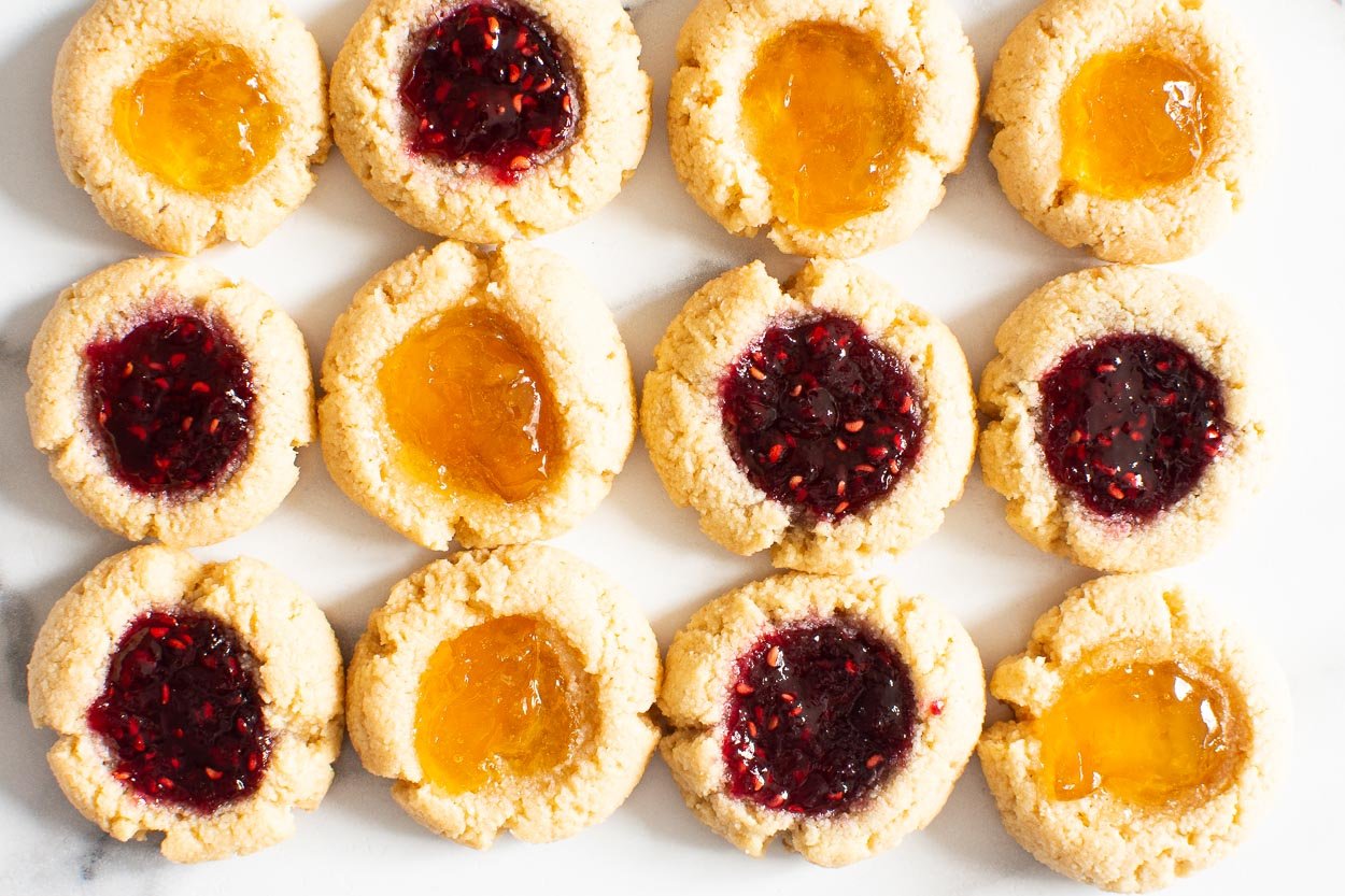 Almond flour thumbprint cookies with raspberry jam and peach jam on a counter.